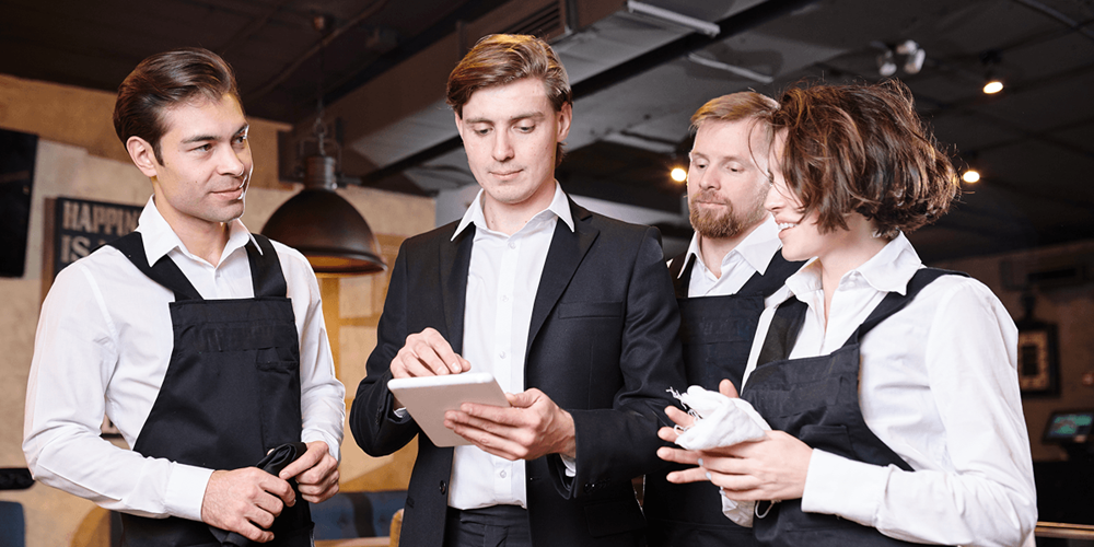Restaurant manager showing AI-generated content on a tablet to three staff members during a pre-service briefing