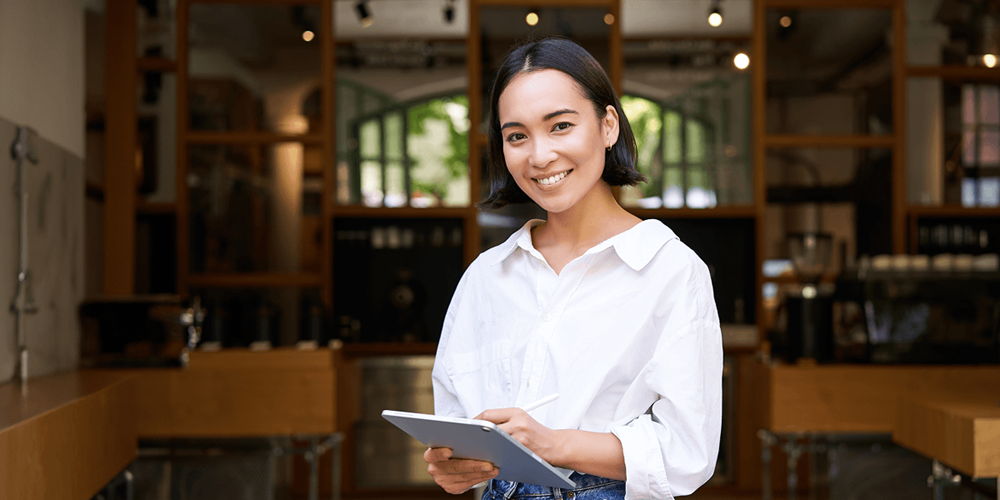 Restaurant manager smiling and holding a tablet in a café, representing tech-enabled daily operations