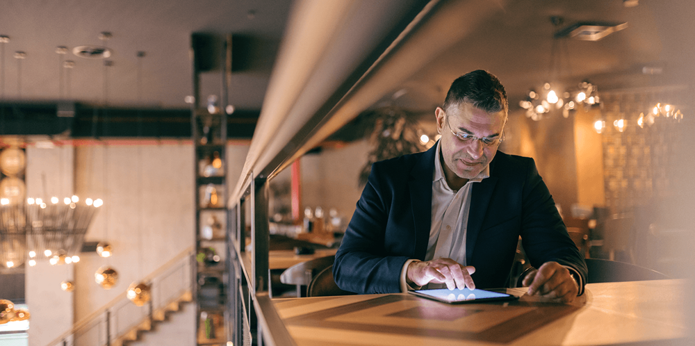 Restaurant manager reviewing data on a tablet at a bar counter during evening service, representing data-driven revenue management