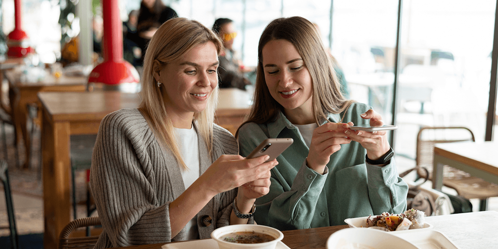 Two guests at a restaurant table sharing content on their phones, illustrating how TikTok drives discovery and word-of-mouth for Gulf restaurants