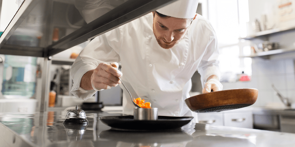 Fine-dining chef carefully plating an orange-glazed dish in a professional kitchen — short clips of moments like this consistently earn high watch-through rates on TikTok