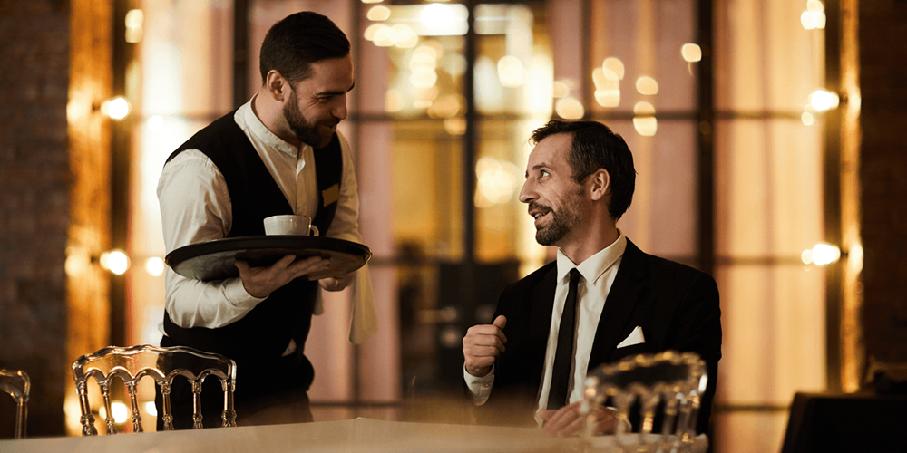 Server attending to a well-dressed guest at a restaurant table — the guest experience moment that payment should never disrupt.