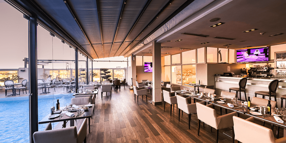 Rooftop restaurant interior with panoramic pool views and a full dining room at golden hour.