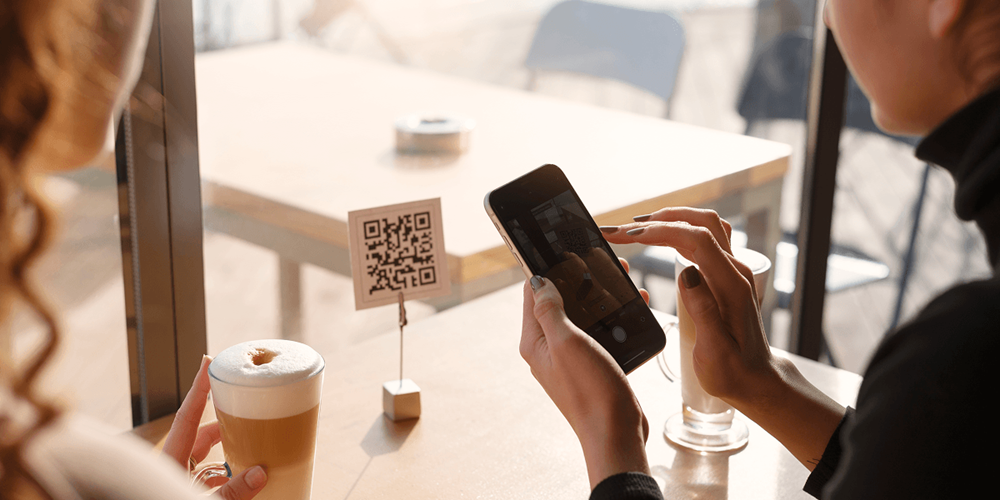 Guest scanning a QR code at a café table to access a digital bill — table-side QR checkout in a casual dining setting.